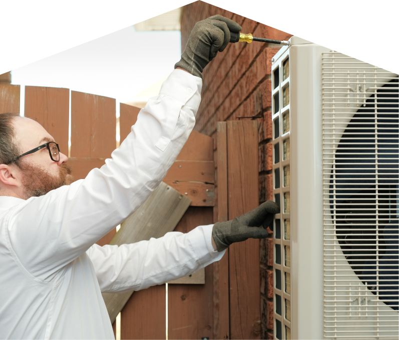 Romaniuk service personnel working on an AC condenser, using a screwdriver to secure the unit’s panel outdoors beside a wooden fence. Romaniuk service personnel working on an AC condenser, using a screwdriver to secure the unit's panel outdoors beside a wooden fence.