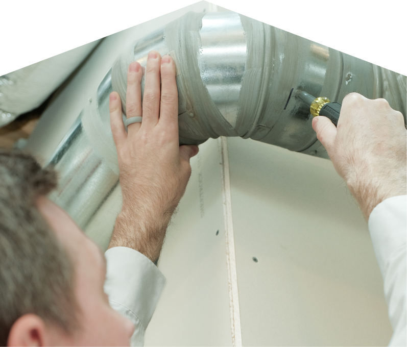 Romaniuk HVAC technician inspecting and tightening a joint on a sealed metal air duct, performing maintenance work during an air duct cleaning task. Romaniuk HVAC technician inspecting and tightening a joint on a sealed metal air duct, performing maintenance work during an air duct cleaning task.