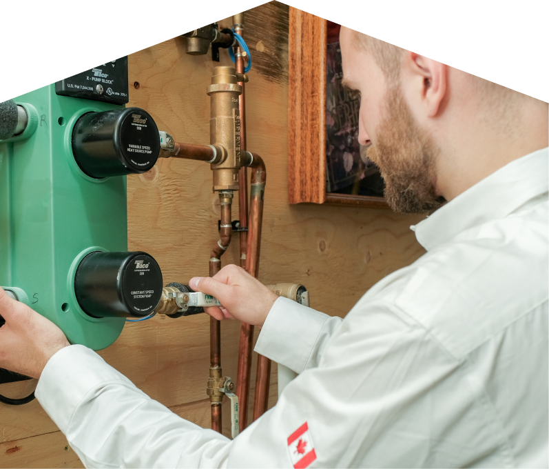 Romaniuk HVAC specialist performing boiler installation, securing a valve on a new hydronic heating system with copper piping and a green circulation pump mounted on a wooden wall. Romaniuk HVAC specialist performing boiler installation, securing a valve on a new hydronic heating system with copper piping and a green circulation pump mounted on a wooden wall.