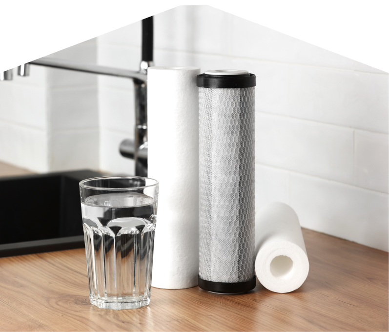 Set of Romaniuk water filtration cartridges placed beside a clear glass of water on a kitchen countertop, with a sink and modern faucet in the background. Set of Romaniuk water filtration cartridges placed beside a clear glass of water on a kitchen countertop, with a sink and modern faucet in the background.