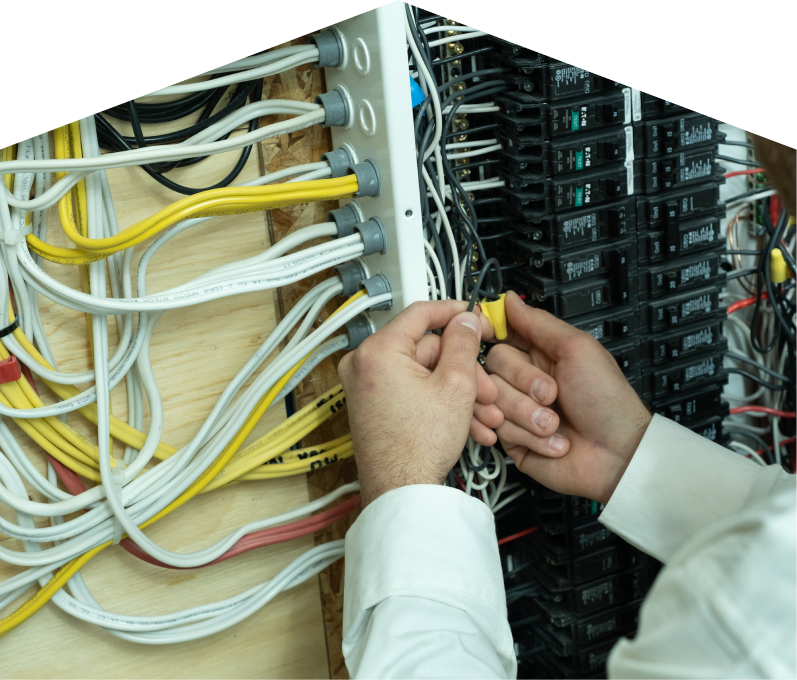 Romaniuk service personnel working on electrical installations, connecting wires inside a residential breaker panel with neatly arranged colored cables on a plywood backing. Romaniuk service personnel working on electrical installations, connecting wires inside a residential breaker panel with neatly arranged colored cables on a plywood backing.