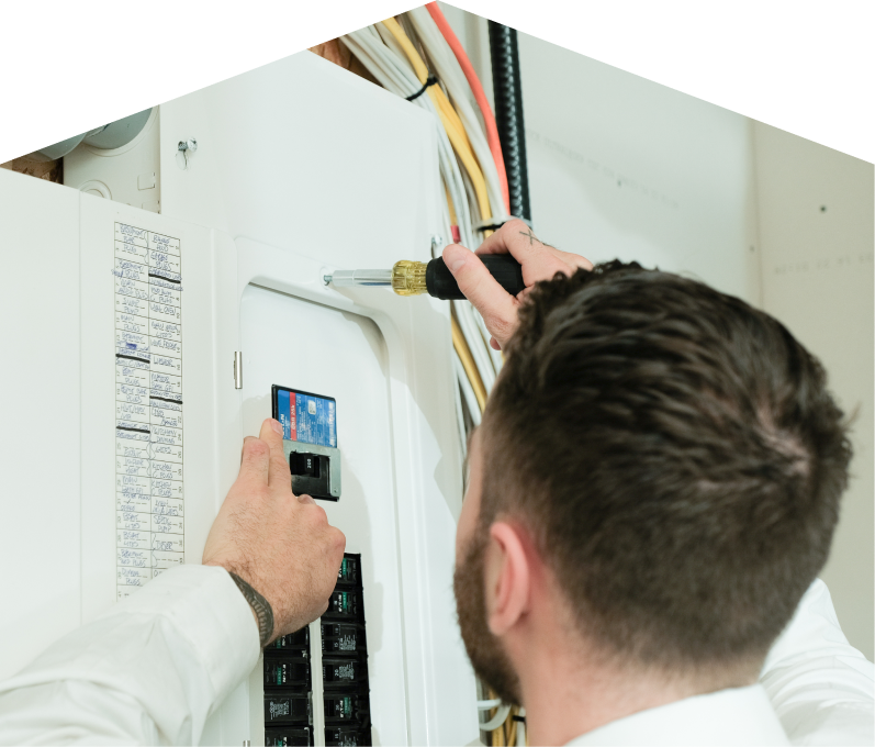 Romaniuk electrician using a screwdriver to perform an electrical panel upgrade, working near organized wiring in a residential wall. Romaniuk electrician using a screwdriver to perform an electrical panel upgrade, working near organized wiring in a residential wall.