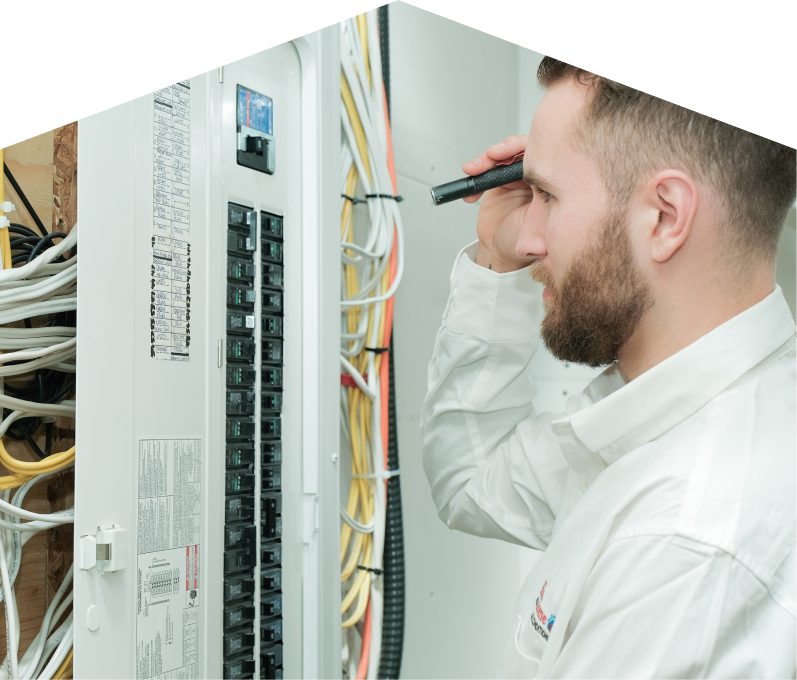 Romaniuk electrician inspecting residential electrical panel wiring with a flashlight, checking connections and circuit labels.