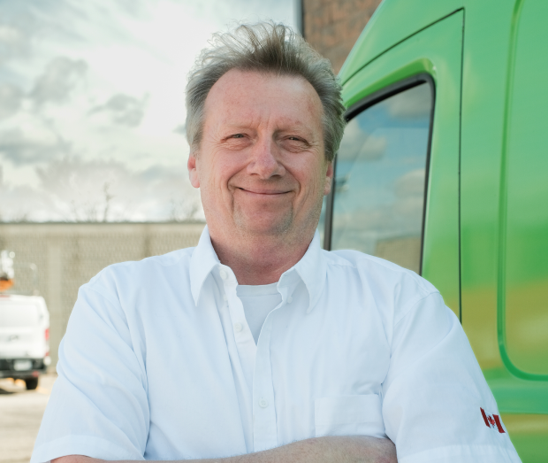 Smiling Romaniuk technician standing confidently in front of their green service van, wearing their white issued uniform. Smiling Romaniuk technician standing confidently in front of their green service van, wearing their white issued uniform.