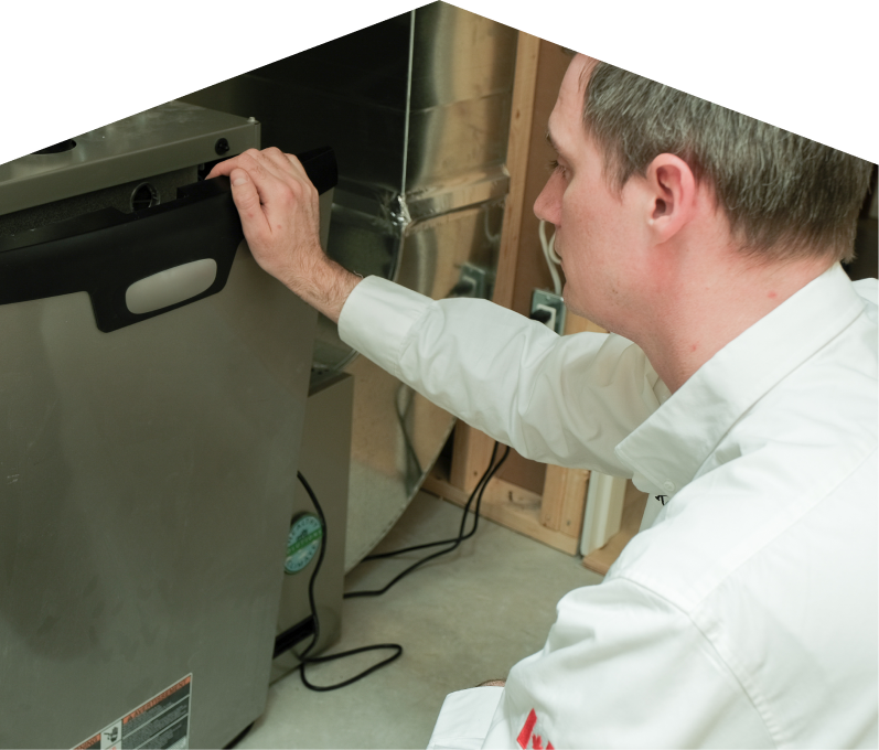 Romaniuk HVAC professional installing a new furnace unit, aligning the front panel with surrounding ductwork and wiring in a residential utility space. Romaniuk HVAC professional installing a new furnace unit, aligning the front panel with surrounding ductwork and wiring in a residential utility space.