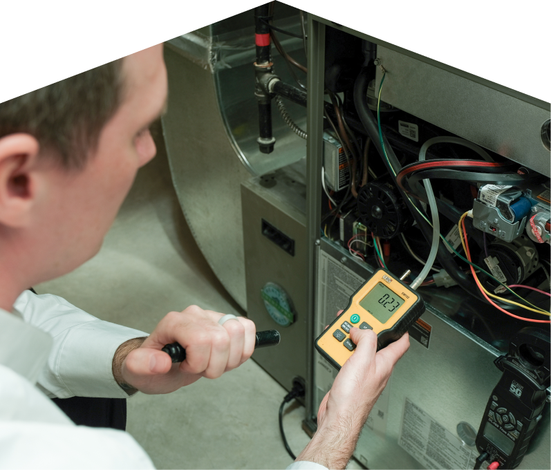 Romaniuk HVAC specialist performing furnace repair on a heating system, using a digital manometer to check pressure. Romaniuk HVAC specialist performing furnace repair on a heating sy