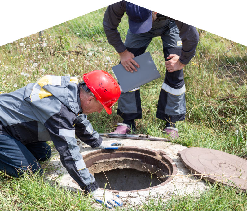 Romaniuk sewer crew inspecting an open manhole in a grassy field, with one member documenting findings on a clipboard. Romaniuk sewer crew inspecting an open manhole in a grassy field, with one member documenting findings on a clipboard.
