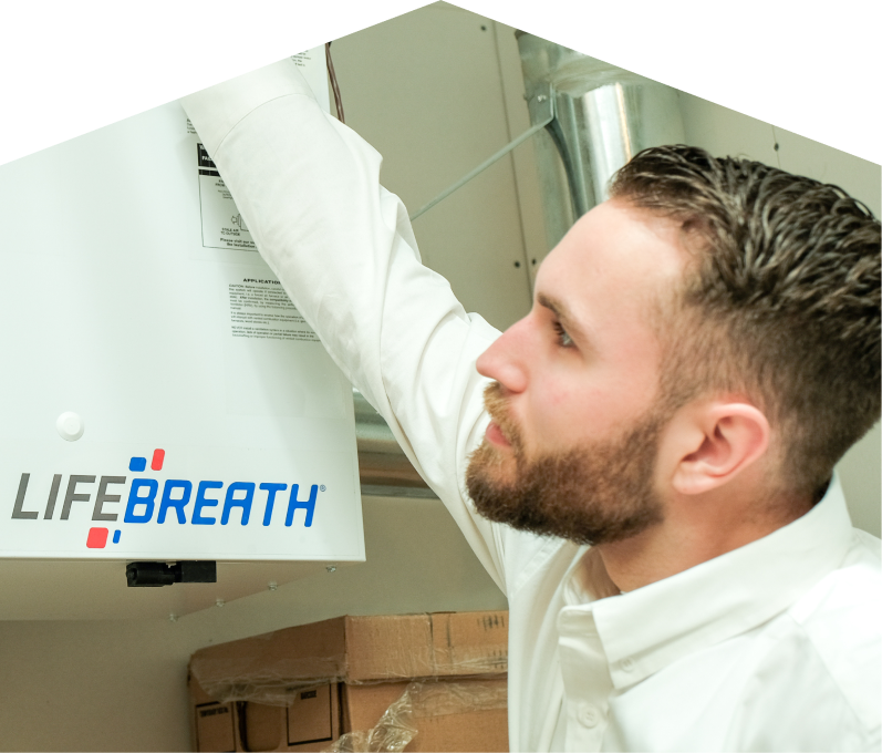 Romaniuk indoor air quality specialist inspects a Lifebreath ventilation unit related to UV air purifiers, with ductwork and boxes in the background. Romaniuk indoor air quality specialist inspects a Lifebreath ventilation unit related to UV air purifiers, with ductwork and boxes in the background.
