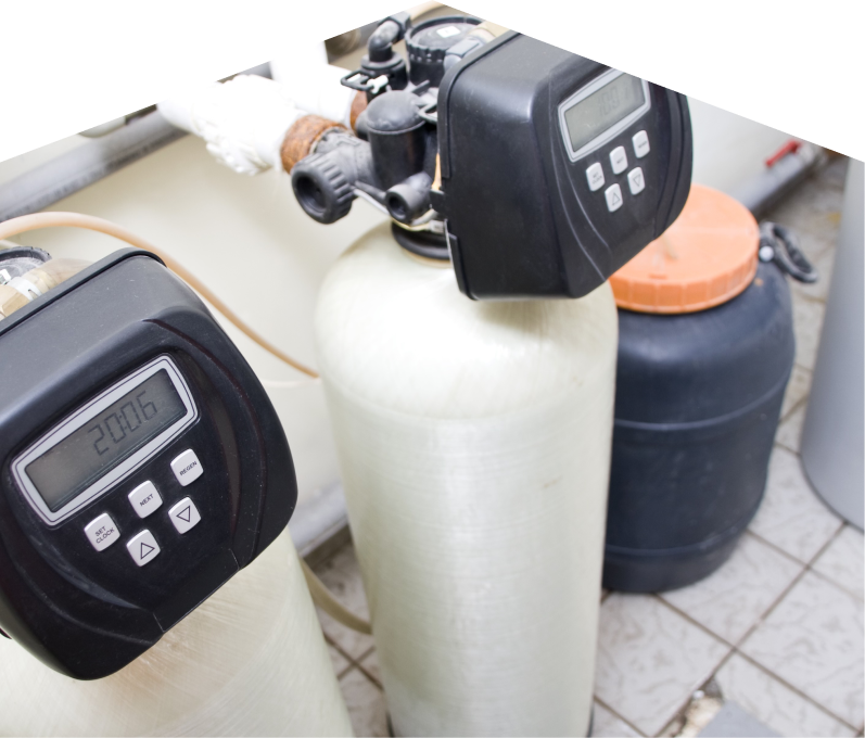 Romaniuk water softener installation showing dual resin tanks with digital control heads and a brine tank in a tiled utility area. Romaniuk water softener installation showing dual resin tanks with digital control heads and a brine tank in a tiled utility area.