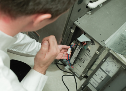 A Romaniuk heating technician inspecting internal wiring during a service check on a residential heating unit. A Romaniuk heating technician inspecting internal wiring during a service check on a residential heating unit.