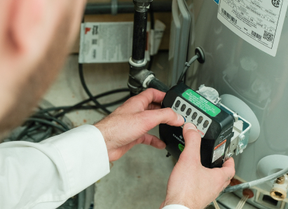 A Romaniuk technician adjusts the control module on a residential water heater, verifying proper operating settings. A Romaniuk technician adjusts the control module on a residential water heater, verifying proper operating settings.