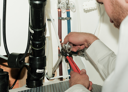 Using two pipe wrenches, a Romaniuk professional plumber services a pipe connection near a vertical flue or vent pipe. Using two pipe wrenches, a Romaniuk professional plumber services a pipe connection near a vertical flue or vent pipe.